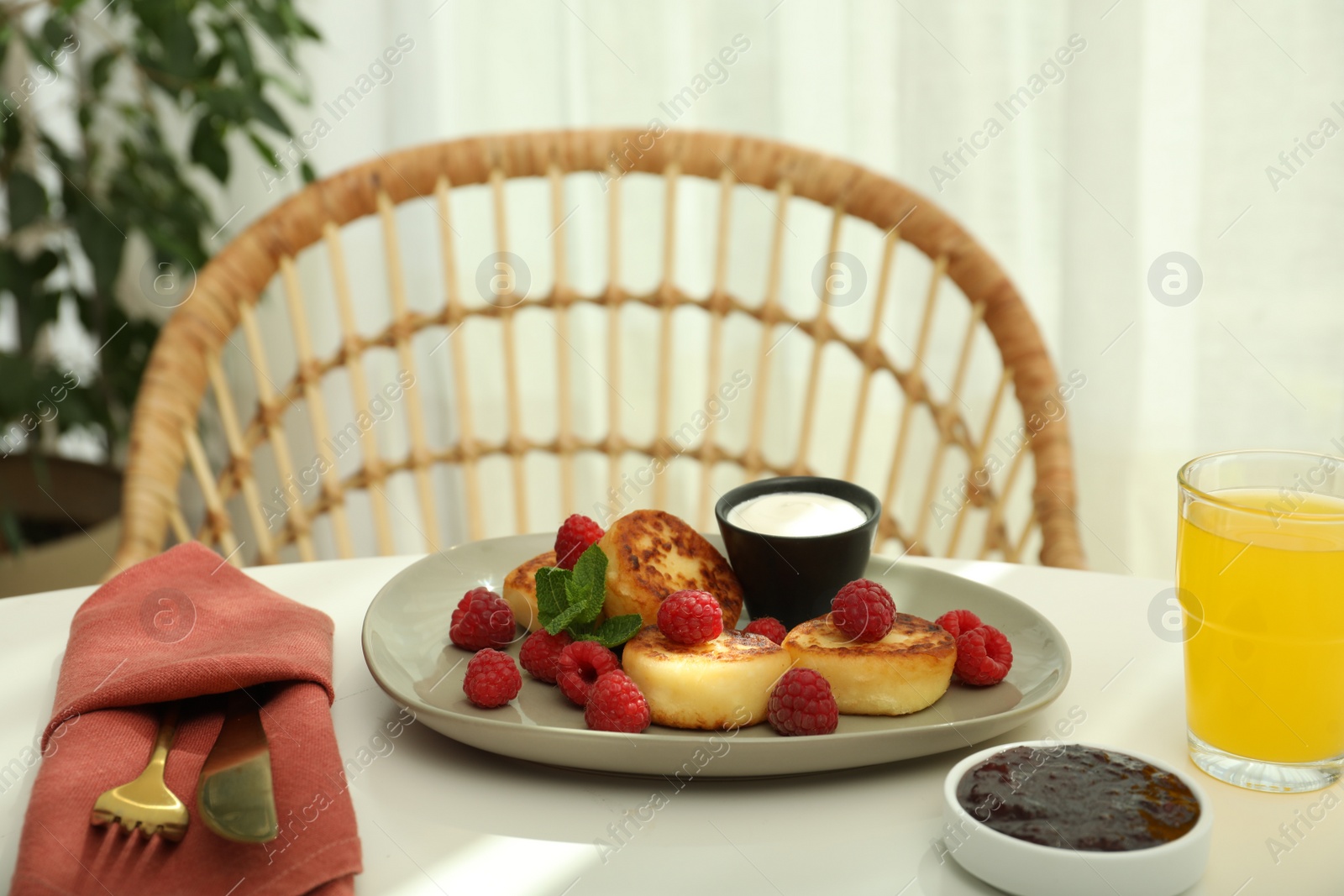 Photo of Delicious cottage cheese pancakes with fresh raspberries, sour cream and mint served on white table indoors