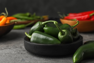 Photo of Black wooden bowl with green hot chili peppers on grey table