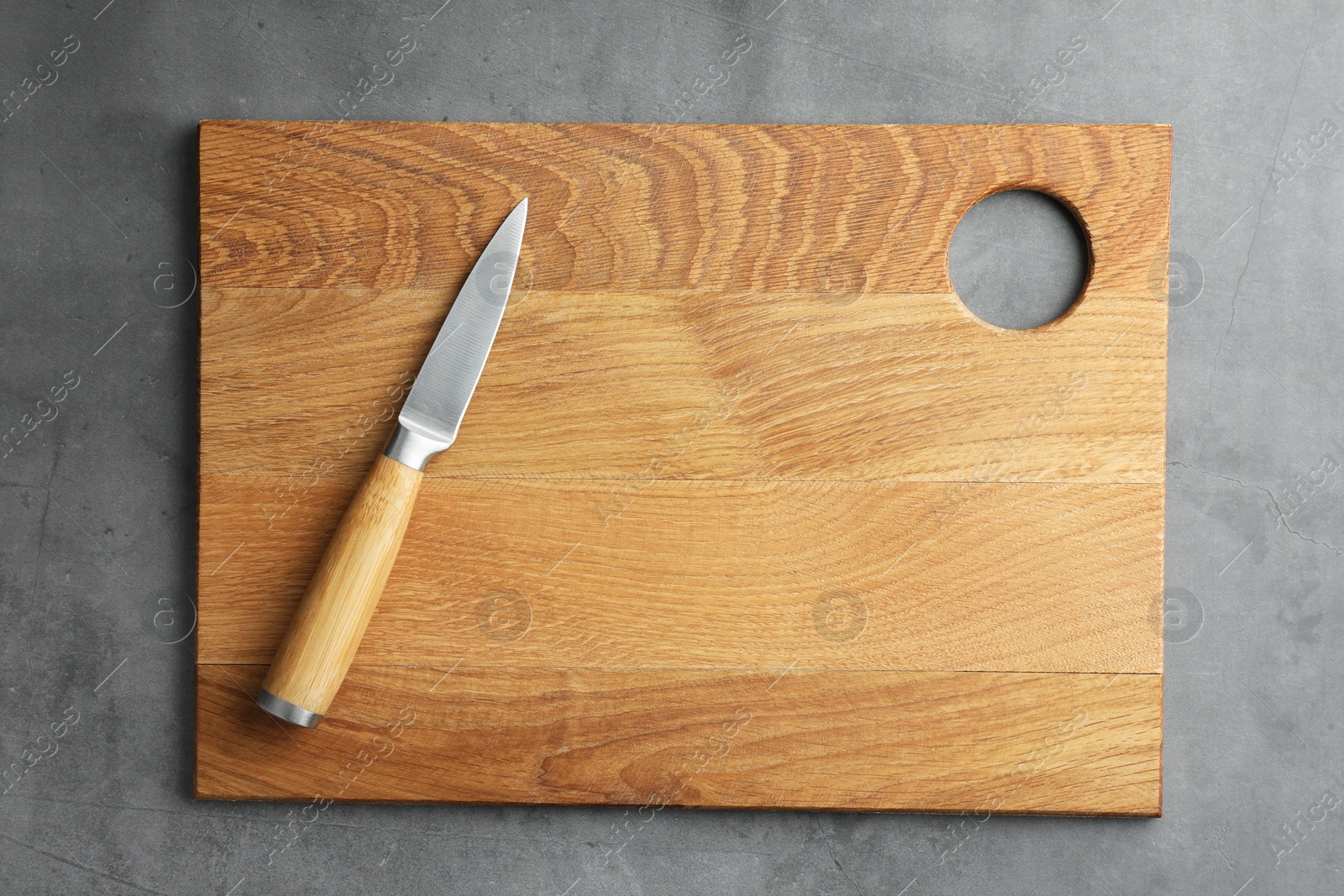 Photo of Knife and wooden board on grey textured table, top view