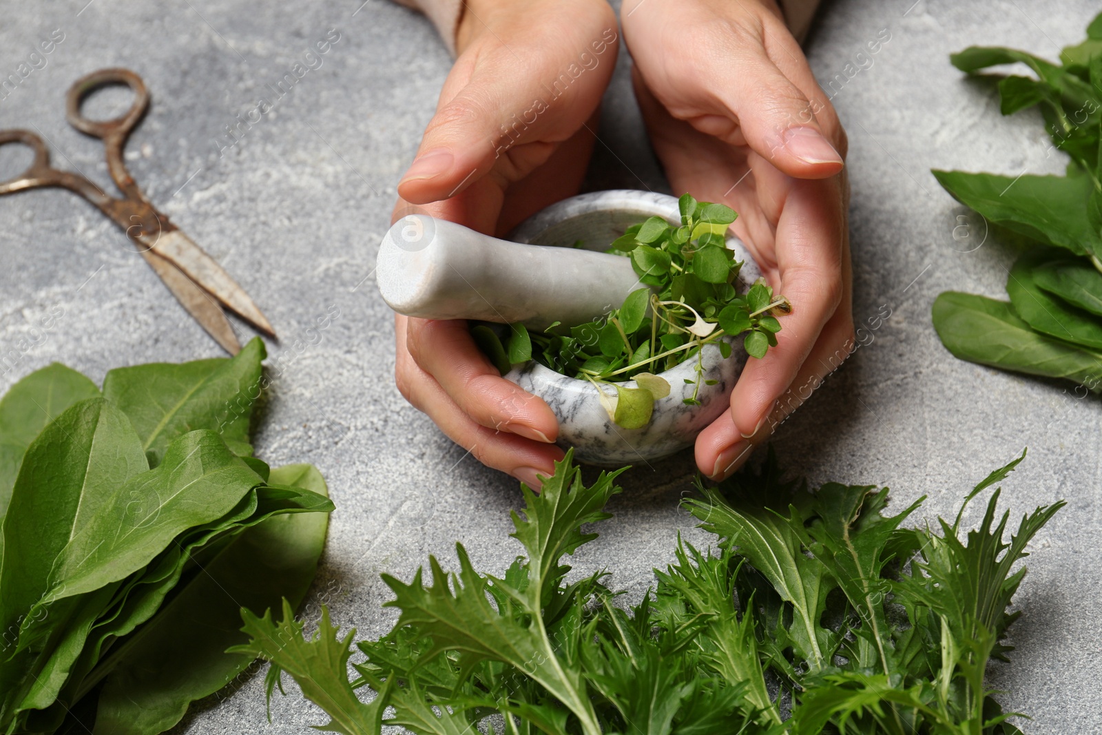 Photo of Woman grinding fresh green herbs in mortar at light grey table, closeup