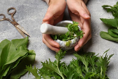 Photo of Woman grinding fresh green herbs in mortar at light grey table, closeup