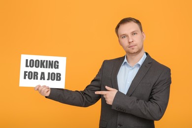 Photo of Unemployed man pointing at sign with phrase Looking For A Job on orange background