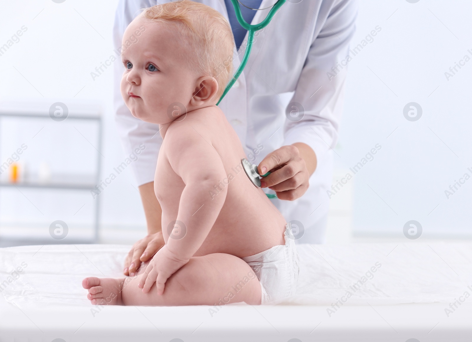 Photo of Children's doctor examining baby with stethoscope in hospital. Space for text