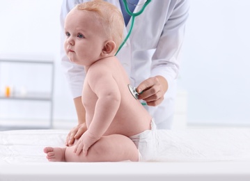 Children's doctor examining baby with stethoscope in hospital. Space for text