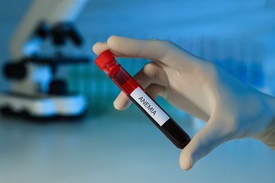 Photo of Scientist holding test tube with blood sample and label Anemia on blurred background, closeup