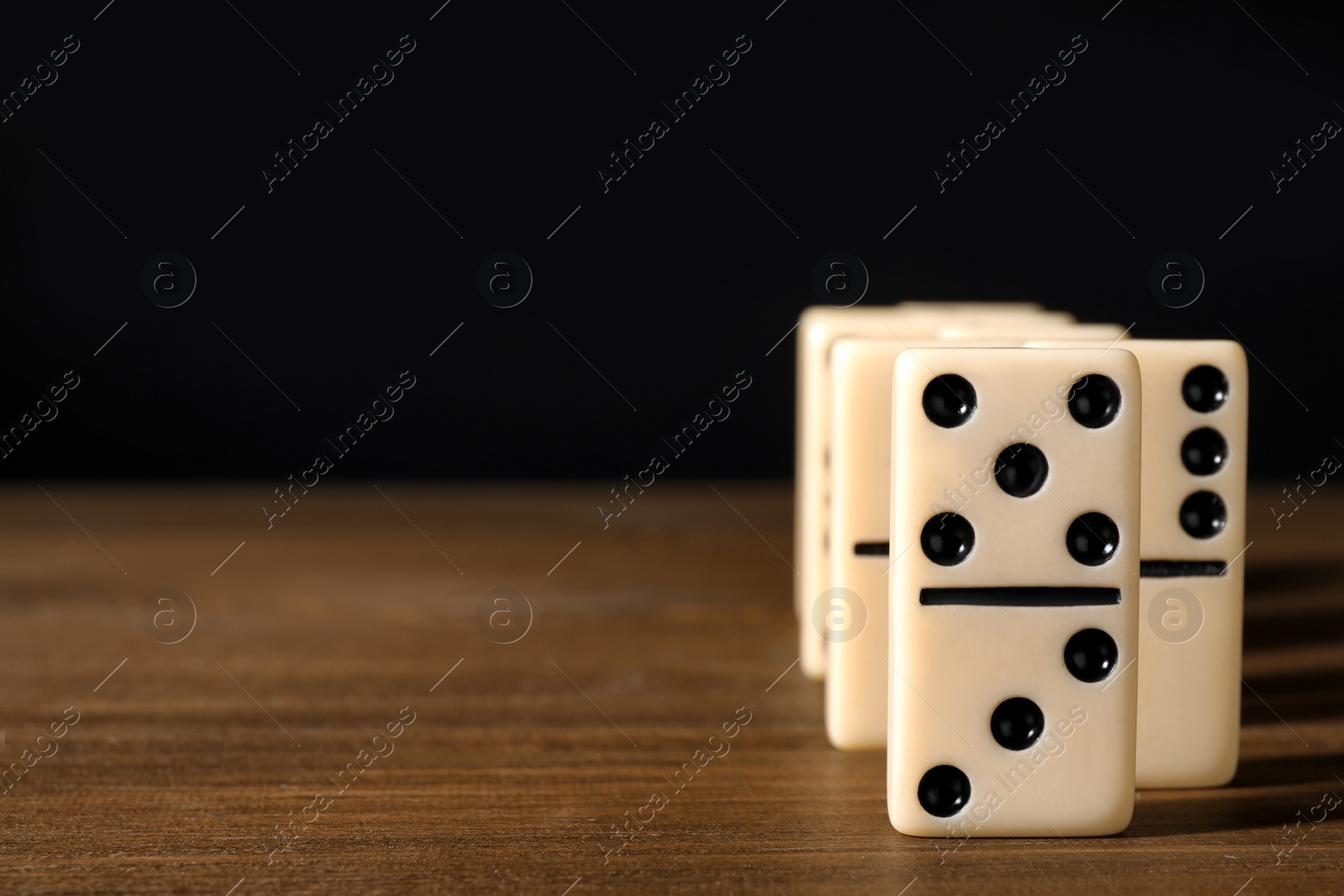 Photo of Domino tiles on wooden table against black background. Space for text