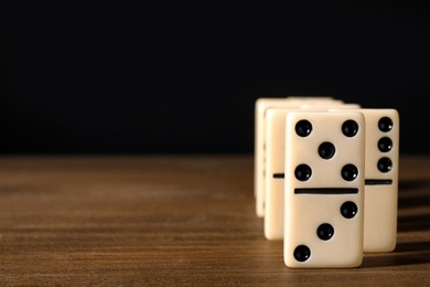 Domino tiles on wooden table against black background. Space for text