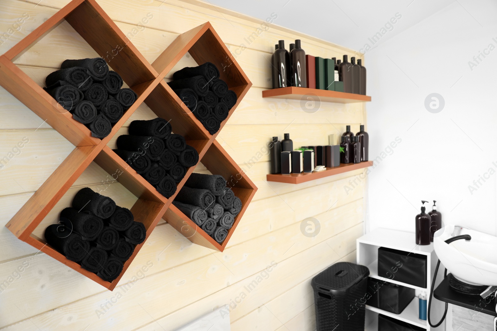 Photo of Shelves with rolled towels and professional hair cosmetics on wall in barbershop