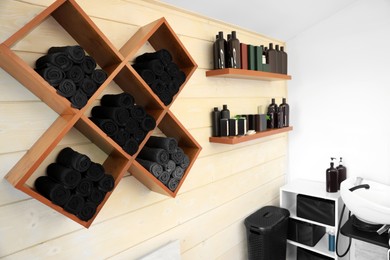 Photo of Shelves with rolled towels and professional hair cosmetics on wall in barbershop