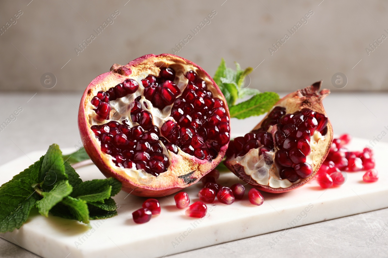 Photo of Ripe pomegranates and seeds on table against light background