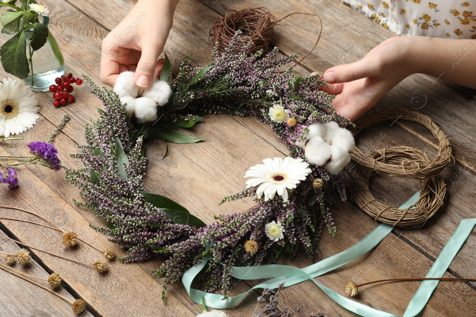 Photo of Florist making beautiful autumnal wreath with heather flowers at wooden table, closeup