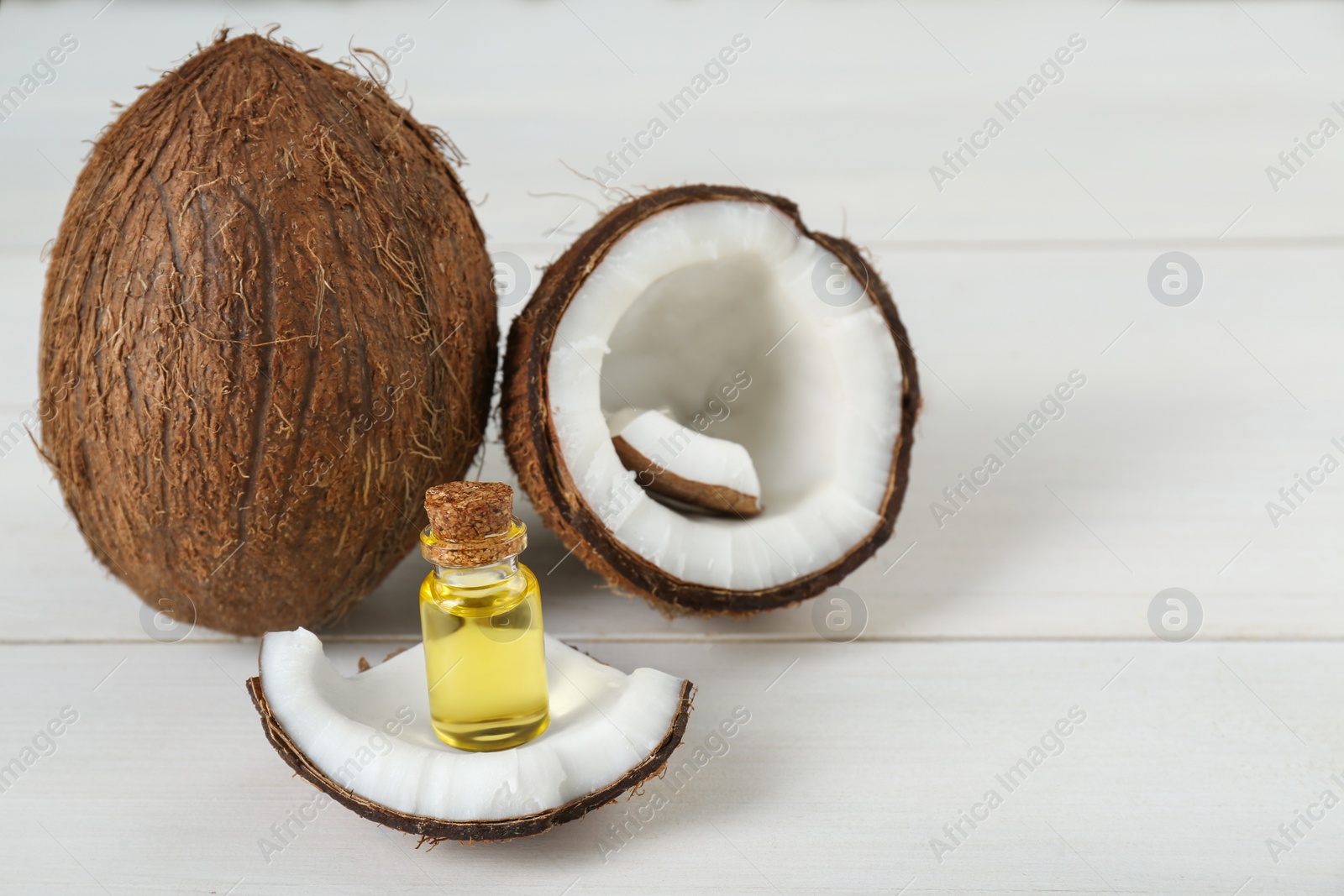 Photo of Bottle of organic coconut cooking oil and fresh fruits on white wooden table, space for text