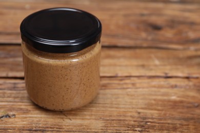 Tasty nut paste in jar on wooden table, closeup. Space for text