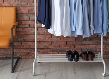 Wardrobe rack with men's clothes and shoes near brick wall