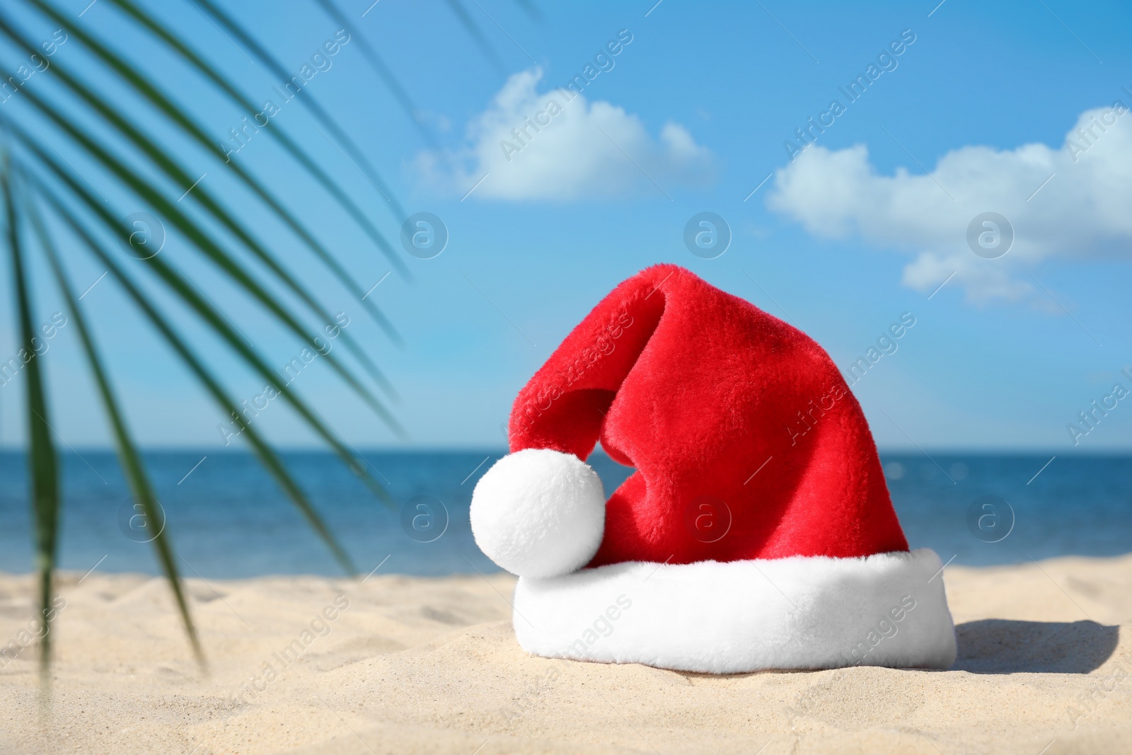 Photo of Santa's hat on sandy beach, space for text. Christmas vacation