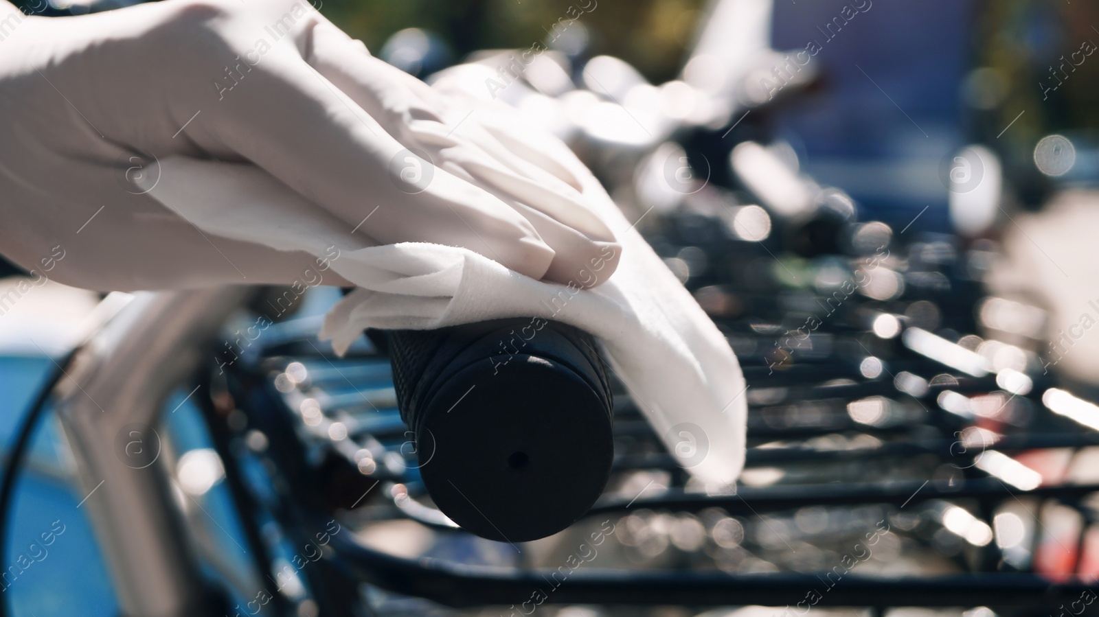 Photo of Woman in latex gloves cleaning bicycle handlebar with wet wipe outdoors, closeup. Protective measures