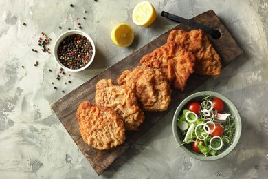 Tasty schnitzels served with lemon and salad on grey table, flat lay