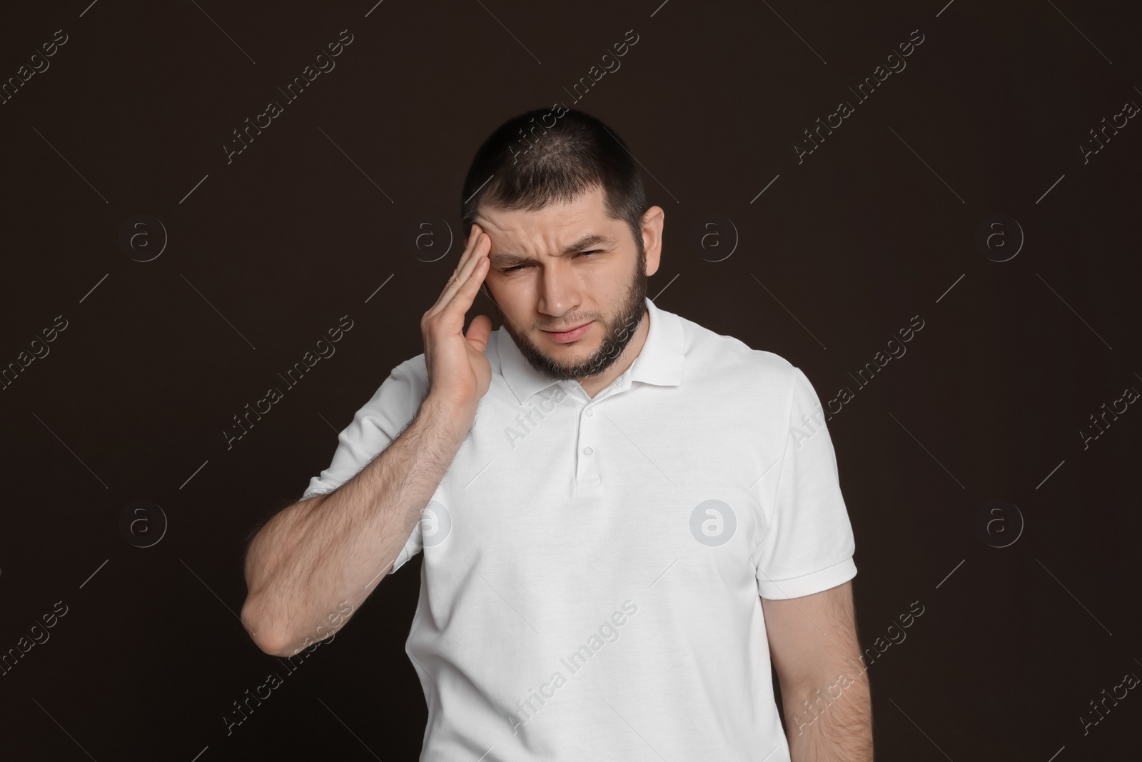 Photo of Man suffering from headache on dark brown background