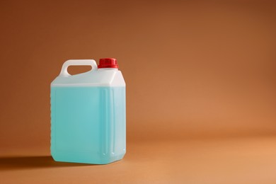 Photo of Plastic canister with blue liquid on brown background. Space for text