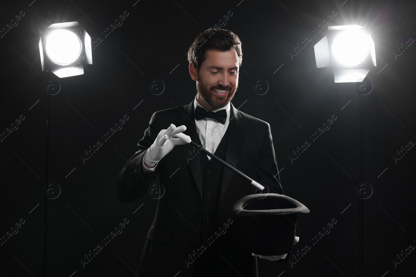 Photo of Happy magician showing magic trick with top hat on stage