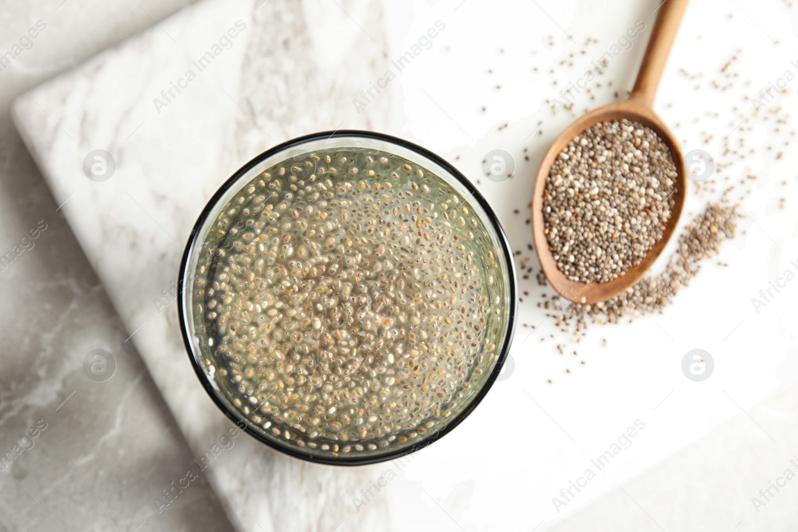 Photo of Glass of water with chia seeds and spoon on board, top view