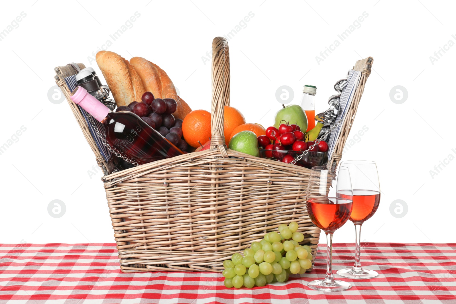 Photo of Wicker picnic basket with different products on checkered tablecloth against white background