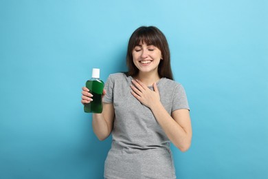 Young woman with mouthwash on light blue background