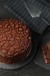 Photo of Delicious truffle cake, server and chocolate pieces on black wooden table