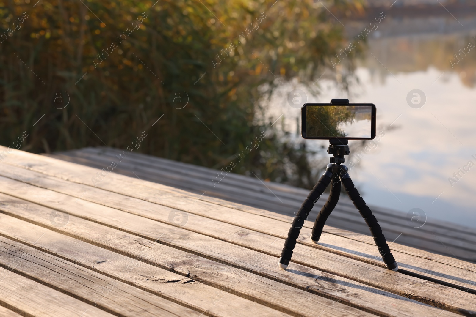 Photo of Tripod with smartphone on wooden pier near river