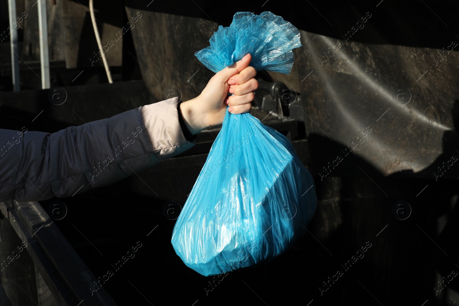 Photo of Woman throwing trash bag full of garbage in bin outdoors, closeup