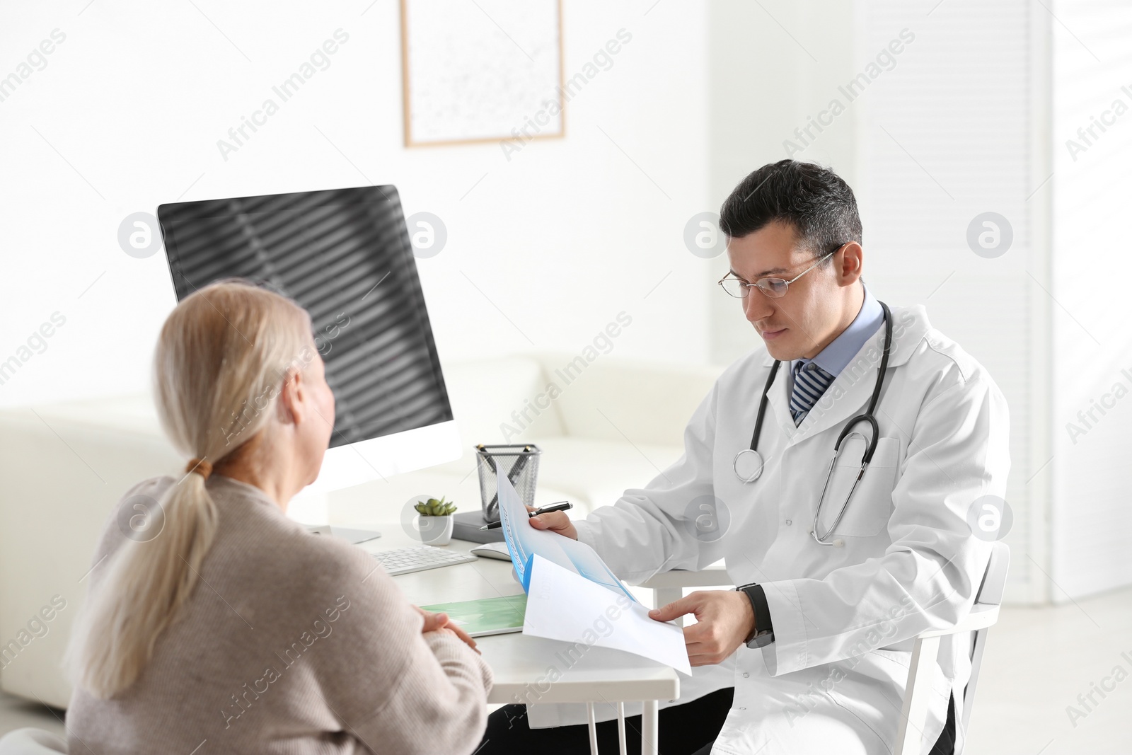 Photo of Doctor consulting patient at desk in clinic