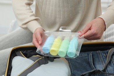 Photo of Woman with plastic bag of cosmetic travel kit packing suitcase, closeup. Bath accessories