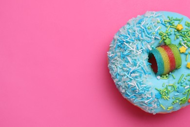 Photo of Sweet glazed donut decorated with sprinkles on pink background, top view and space for text. Tasty confectionery