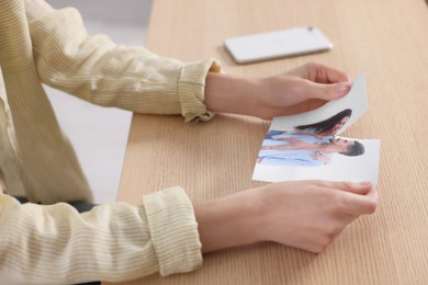 Woman holding torn photo at wooden table, closeup. Divorce concept