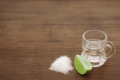 Photo of Mexican tequila shot with lime slice and salt on wooden table, space for text. Drink made from agave
