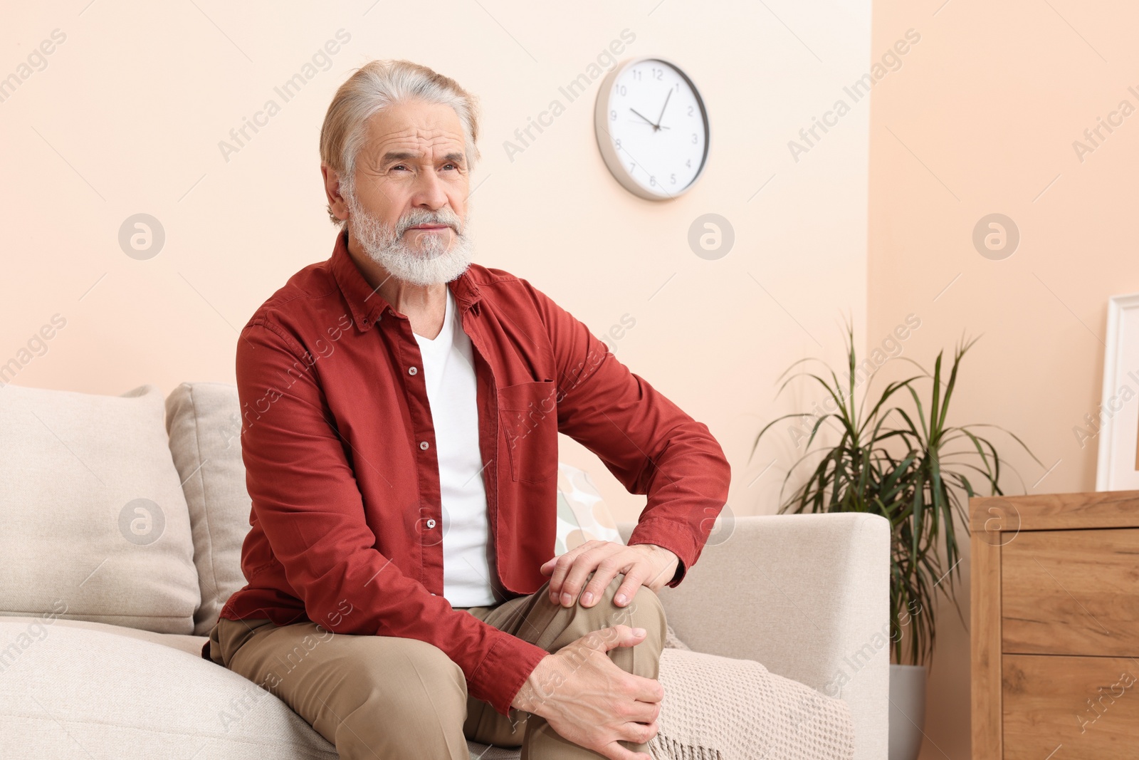 Photo of Senior man suffering from pain in his knee at home. Arthritis symptoms