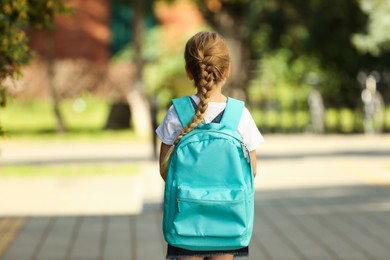 Photo of Little girl with turquoise backpack going to school outdoors, back view