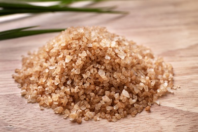 Photo of Pile of brown sea salt on wooden table, closeup. Spa treatment