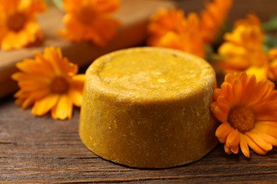 Yellow solid shampoo bar and flowers on wooden table, closeup. Hair care