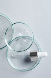 Photo of Petri dishes with samples of cosmetic oil and pipette on white background, flat lay