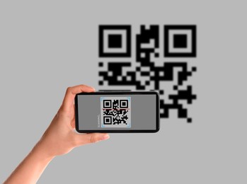 Image of Woman scanning QR code with smartphone on light background, closeup