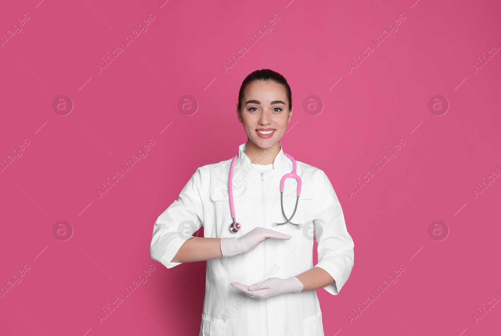 Photo of Beautiful young doctor holding something on pink background