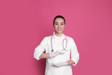 Photo of Beautiful young doctor holding something on pink background