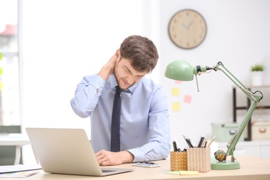 Young man suffering from neck pain in office