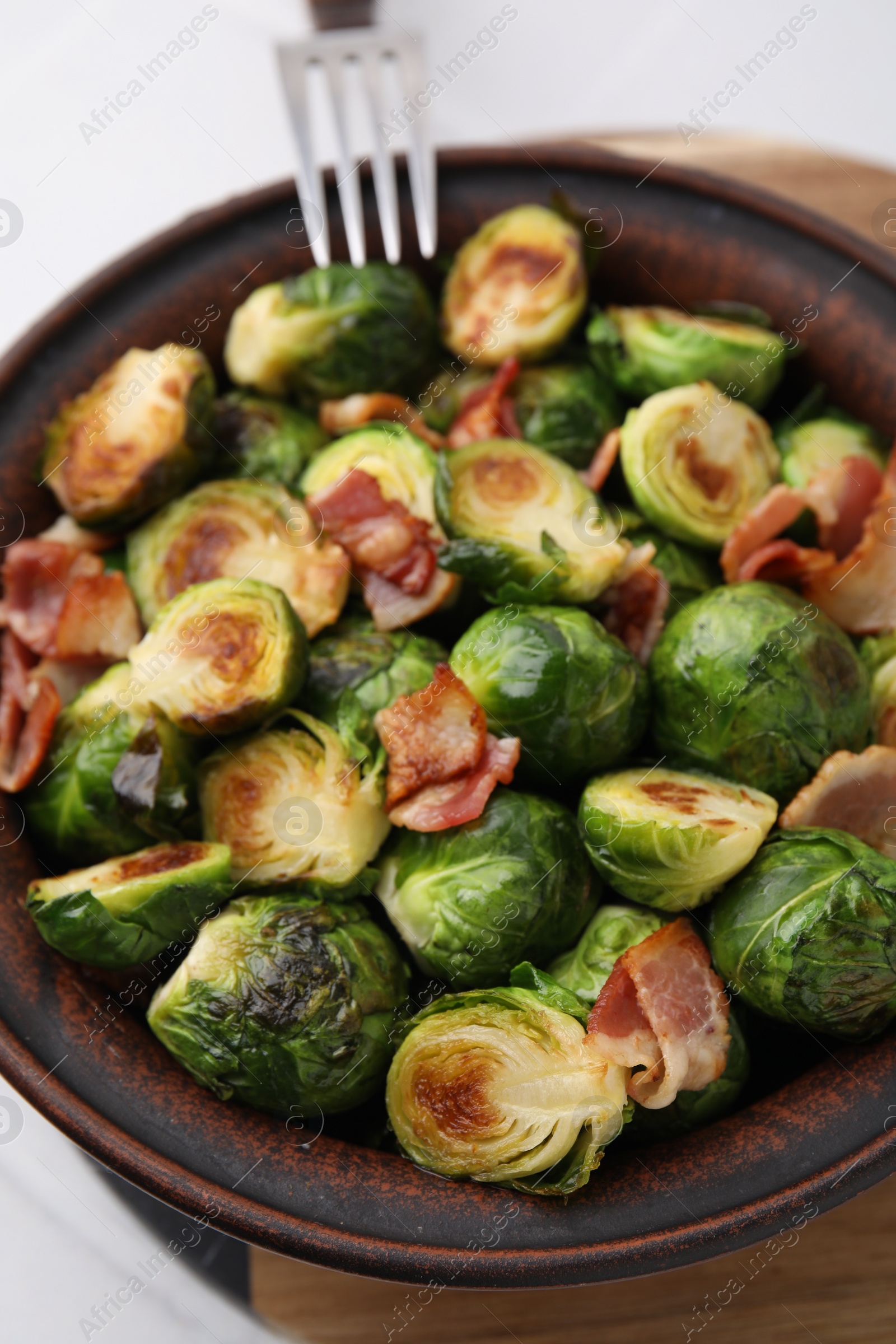 Photo of Delicious roasted Brussels sprouts and bacon in bowl on table, closeup