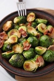 Photo of Delicious roasted Brussels sprouts and bacon in bowl on table, closeup