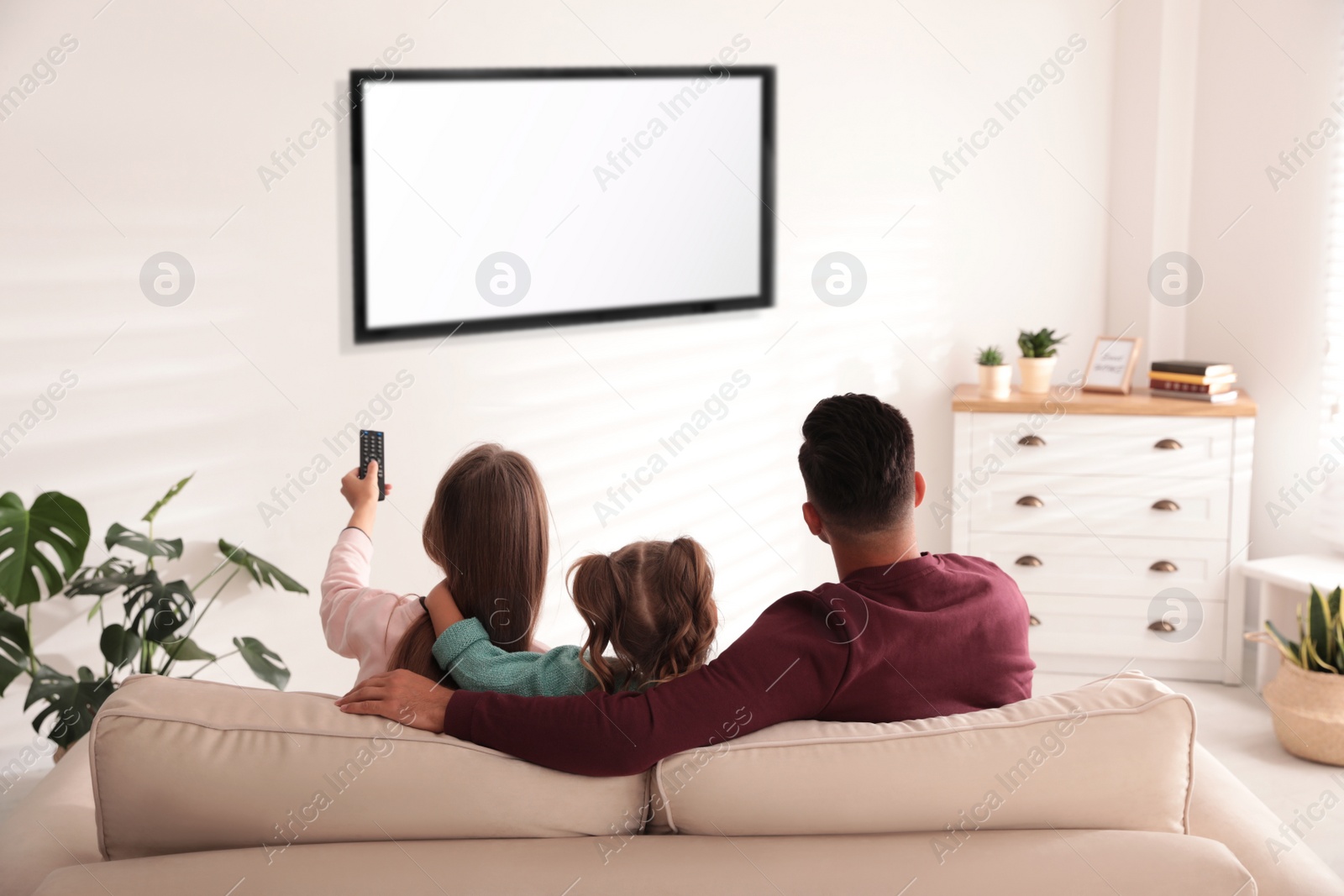 Photo of Family watching TV on sofa at home, back view