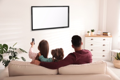 Photo of Family watching TV on sofa at home, back view