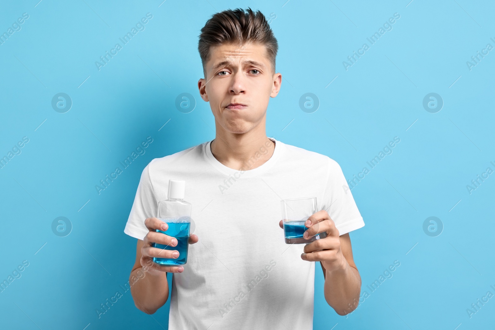 Photo of Young man using mouthwash on light blue background