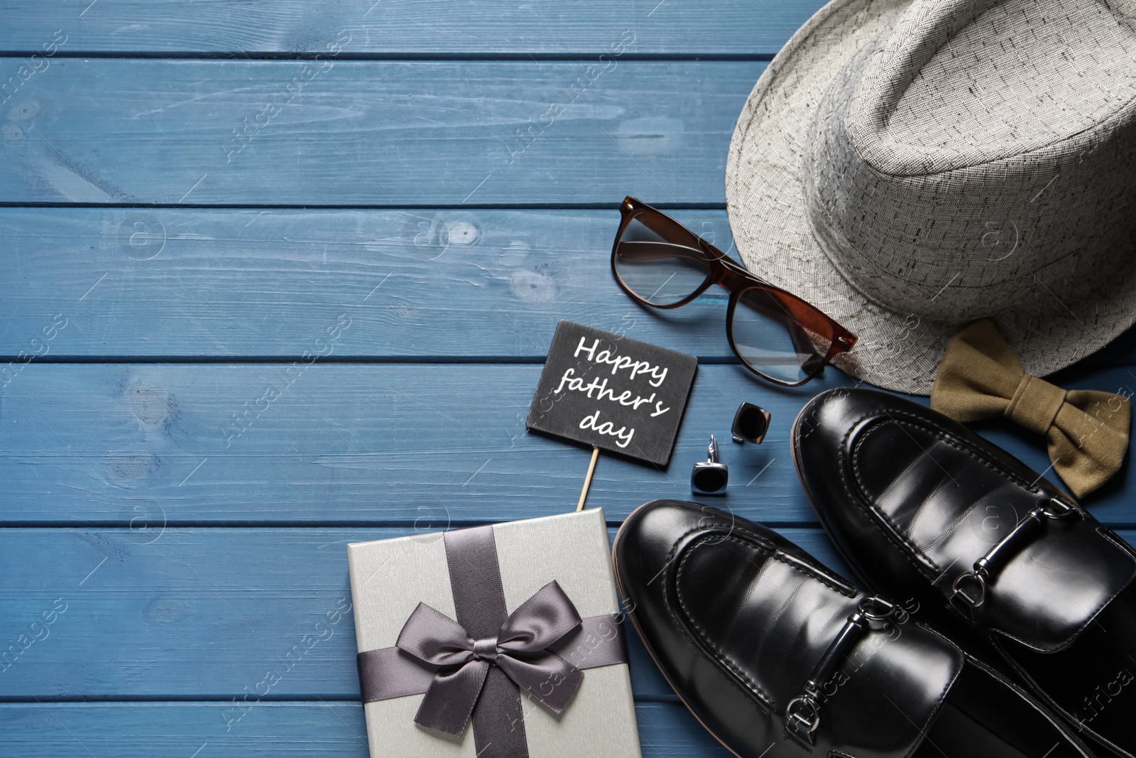 Photo of Card with phrase Happy father's Day, shoes, gift box and different men accessories on blue wooden background, flat lay. Space for text